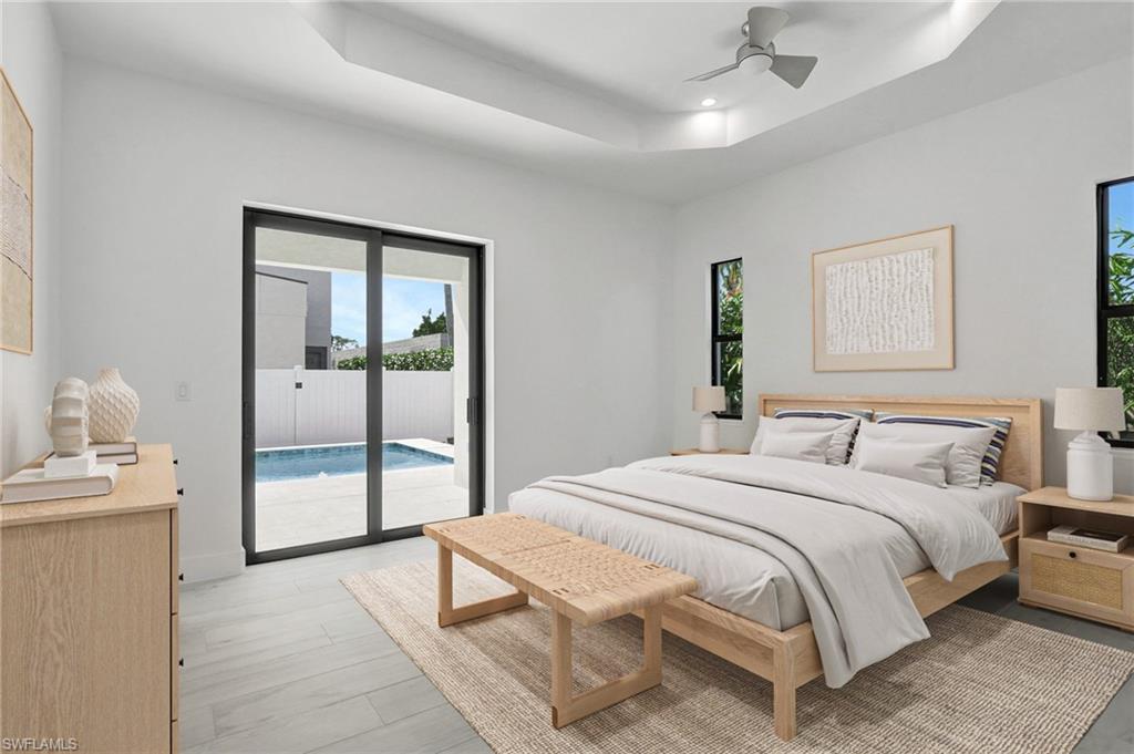 Modern bedroom featuring a large bed with light bedding, natural wood furniture, and sliding glass doors leading to a private pool area in a newly constructed luxury home in Naples Park, Florida.
