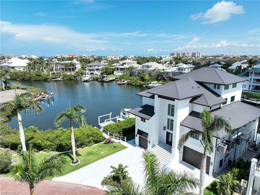 This 4-story Bayfront Gardens home features an exquisite coastal style & is located on one of the finest waterfront lots in double gated Bayfront Gardens with an incredible bayfront setting with 265’ of waterfront.  This stunning home has five bedrooms, 5.5 baths, impact windows & standing seam metal roof. The designer touches are endless & include light oak wood flooring, granite countertops, marble backsplashes, Thermador appliances, marble baths, quality mill work & cabinetry, main floor master suite and guest suites the size of a master bedroom, and the ultimate garage! Light, bright & airy along with an idyllic western exposure setting that offers beautiful sunsets over the Gulf of Mexico from your 4th floor covered deck. The exterior features an amazing pool & spa that sits right on the water, two new docks with lifts, composite decking, nautical rope railings, marble driveway & pool deck, a preserve across the street, & a dedicated beach access a short walk away. If you are looking for a house that needs no renovations, current style & floor plan, move in ready, w/furnishings available, beach, boating, wide water views, sunset, gated & security patrols this it it!