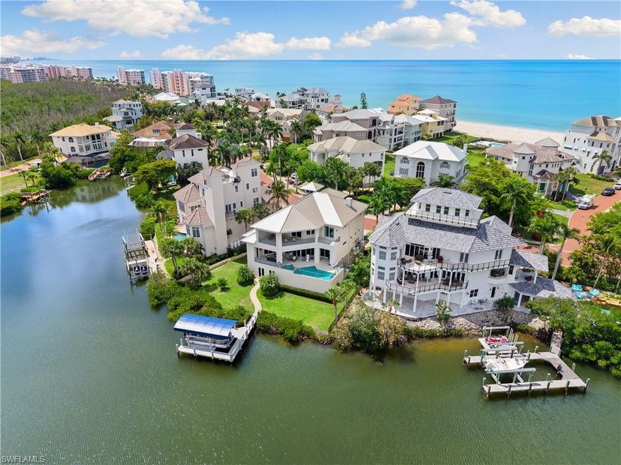 Stunning bayfront masterpiece with sweeping water views in North Naples’ premier community of Barefoot Beach. A true boater and beach lover’s paradise, this exceptional home offers direct Gulf access from your private dock with a brand-new covered boat lift (2025) and deeded beach access just a 5-minute walk away. Perfectly positioned to capture breathtaking bay views, this home showcases expansive fully pocketing sliders that create a seamless indoor-outdoor living experience. Built like a fortress, this residence is crafted with a metal roof, electric hurricane shutters, and hurricane-impact windows and doors. Spanning 5,187 sq ft under air, this thoughtfully designed residence features 5 bedrooms, 4 full bathrooms, 2 half bathrooms, a 3-car garage, private elevator, and two new HVAC systems (2026). The beautifully appointed interior includes engineered maple hardwood flooring, soaring tray ceilings with custom accents, a newer whole-home audio system, and Lutron lighting throughout. The stunning chef’s kitchen features quartz countertops, white cabinetry, Thermador and Sub-Zero appliances including a 6-burner Thermador gas range, a double wall oven, and an adjacent dining area. Entertain effortlessly with a stylish wet bar complete with Vetrazzo counters and a dual-temperature Sub-Zero wine cooler. The luxurious primary suite offers private access to the lanai and serene water views, along with a spa-like bathroom featuring dual vanities, a soaking tub, and an expansive frameless glass walk-in shower with a rainfall showerhead. Outdoor living is designed for relaxation and entertaining, highlighted by an elevated pool and spa overlooking the bay, a spacious lanai, a fully equipped outdoor kitchen with a gas grill, a pool bath, and pool equipment elevated approximately three feet. Additional features include a Generac whole-home generator, 500-gallon propane tank, electric screens, bonus room/flex space with wet bar, and a private top-floor balcony with elevated bay views. Optional membership to the exclusive Club at Barefoot Beach provides access to tennis, two restaurants, and beachside/poolside food and beverage service. Ideally located near world-class dining, shopping at Mercato and Waterside Shops, RSW International Airport, and just a short drive to the renowned Fifth Avenue South in Naples.