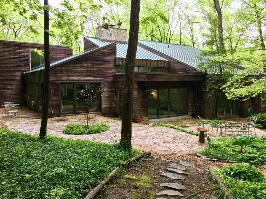 This Sugar Creek Valley home was designed to be “green”.  Featuring vaulted ceilings, triple pane sliding glass doors and angles that catch the winter sun in every room.  The beautiful surrounding woods create shade in the summer and every room opens to a patio or deck.
Designed by Tom Hall this 3,081 sq. ft. home on 1.4 acres has a copper roof and natural cedar siding. Flagstone is used abundantly at the entrance, on the fireplace walls, the raised patio off of the atrium and the two level patio off of the dining room and kitchen.
The master bedroom suite has his and her bathrooms and closets.  Second bedroom suite has a roof top deck. Third bedroom suite is multileveled. 
Custom cabinetry in the vaulted kitchen creates exceptional storage behind the wall of eight ft. high doors.
Contemporary today as the day it was built. Agt related