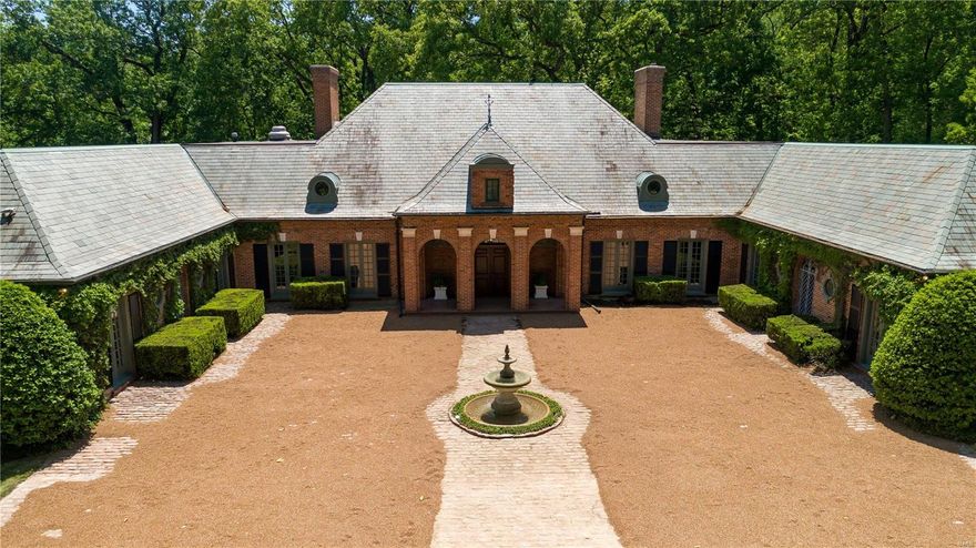 A dramatic Southern France-inspired Ladue Estate approached by walled forecourt, paved in cobblestones, with garden facades and round windows. Slate roof with dormers and stone keystones accentuate entrance porch with three arched openings. The interior introduces rustic forms and materials in a casual atmosphere while retaining the formality of crystal chandeliers and marble mantle pieces. Sunken Living Room with carved marble mantle parallels the rough-hewn beams and etched leaded glass window defining Hearth Room. Entrance loggia crosses front of house in a long axis at right angle to principal rooms plus two first floor Master Suites, each with Master Bath and Dressing Room, en suite Guest Quarters and full In-law Suite. Additional 3 bedrooms are located on upper level. Other features include turreted Carriage House apartment, 6 heated garage bays, pool accented by authentic thatched roof huts, large screened porch with brick patio. Home is situated in wooded 3.12 secluded acres Additional Rooms: Sun Room