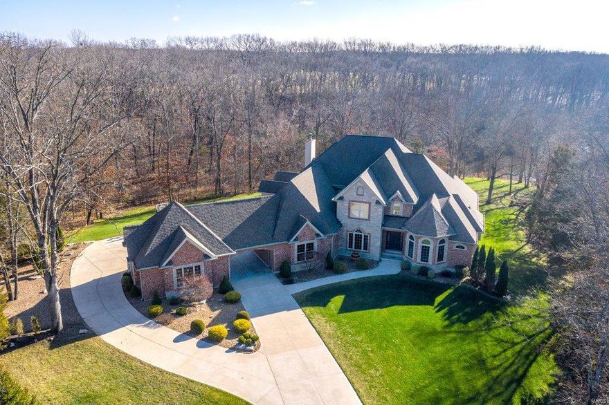 Spectacular brick & stone 1.5-Sty on 3.4 acre grounds! Distinctive design elements including handscraped hardwood flooring, soaring ceilings, architectural columns & arched entryways are evident throughout the home. Impressive 2-sty foyer leads to private study, elegant dining and stunning great room with dramatic wall of windows overlooking the lake. Designer kitchen with 42” maple cabinetry, granite countertops, 9’ center island & butler’s pantry adjoins light-filled breakfast room & hearth room highlighted by floor-to-ceiling brick & stone fireplace. Coffered master bedroom suite combines the enjoyment of a direct vent fireplace with sitting room & luxury bath. Oak staircase accesses 3 additional bedrooms, 2 with Jack n’ Jill bath, hall full bath, bonus room & 2nd laundry. Walk-out Lower Level includes recreation room with wet bar, family room, hot tub room, workout room & full bath. Situated on a wooded cul-de-sac lot with deck, patio & pool plus 2 & 3-car garages & porte cochere.