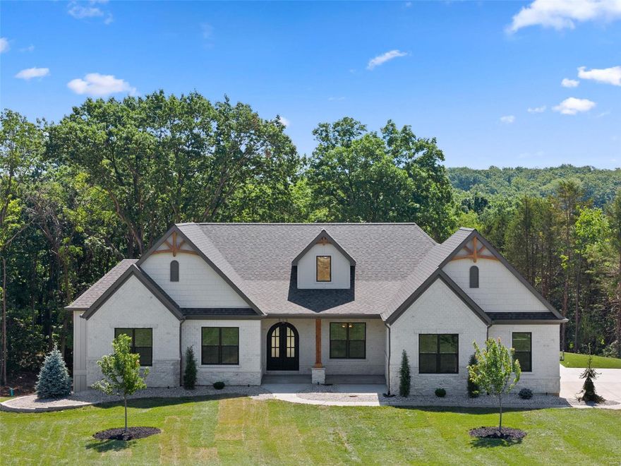 Stunning custom spec home on 3+ acre wooded lot in new St. Charles Co development. Home trimmed w gorgeous stained white oak flooring & 6 1/4" baseboards. Great Room stone fireplace w gas insert flanked w built-in bookcases & highlighted by natural light from expansive wall of windows. Kitchen features quartz counter tops, soft close cabinets w crown molding, under cabinet lighting, tile backsplash, walk-in pantry. Owner's suite features spacious bedroom w coffered ceiling, 14x8 closet, luxury bathroom w fluted glass door, double vanities, separate free-standing tub & tiled shower. Two additional bedrooms, home office w glass french doors, full bath, powder room & laundry complete the main floor. Laundry room features closet, cubbies, cabinetry & sink. Beautiful brick & stone front elevation w iron arched entry door & 16x16 covered patio. 9' basement pour. Upgrades include: 8' doors, additional windows, high end appliances, custom pantry & closets, basement finish & more!