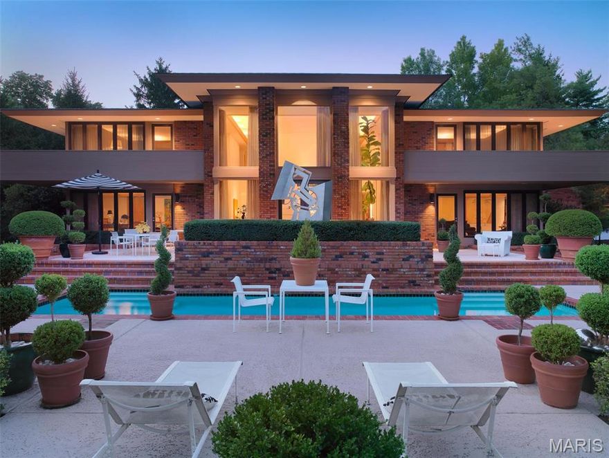 Nestled on nearly an acre in Ladue and surrounded by the tranquil Carmelite Monastery, this modern Bernoudy-inspired home is a serene retreat with luxurious design. At its heart is a dramatic two-story family room featuring a wood-burning fireplace and seamless access to the pool, perfect for entertaining. The sleek eat-in kitchen boasts marble countertops and white cabinetry. A formal dining room and elegant living room provide additional entertaining options. The primary suite offers a private deck, a marble-clad bathroom with dual vanities, a tub, a shower, and a spacious walk-in closet, all overlooking the landscaped backyard and pool. Two additional bedrooms, one serving as a den and a full bathroom, complete the upper level. With a 2-car garage and a prime location near Truffles, Palm Health, and Kaldi’s, this home combines privacy, modern living, and convenience.