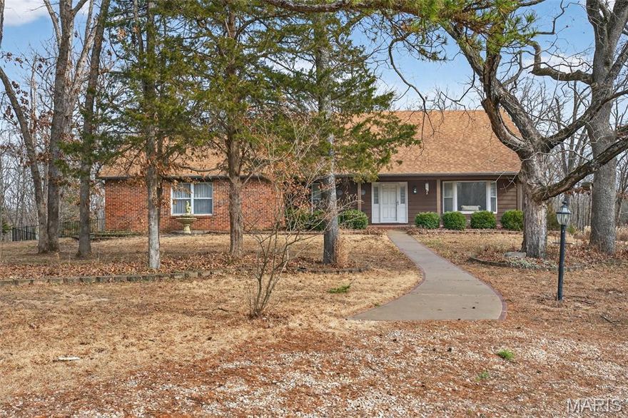 This is the one you've been waiting for! Set on 14 scenic acres with approximately 5 acres cleared, this spacious 3,430 square foot home offers privacy, versatility, and easy highway access, located about an hour from St. Louis. An electric gate at the entrance provides added security and privacy, while a circle drive creates a welcoming arrival to your homestead oasis.
Inside, vaulted ceilings and sun-filled rooms create a warm, open feel. Hardwood floors run throughout much of the home and are complemented by two fireplaces, including a brick hearth centerpiece in the great room & another in the basement. The living and dining rooms are ideal for entertaining, while sliding glass doors open to a bright three seasons room overlooking the park-like backyard. 
The kitchen features double ovens, ample cabinetry, generous counter space, and a breakfast area. The main-floor primary suite includes a walk-in closet, private bath, and French doors leading directly into the solarium. The solarium also offers the rare benefit of its own basement, separate from the main house basement.
Upstairs, you will find three additional bedrooms with hardwood floors and large closets, along with a full bath. The walk-out basement provides a spacious recreation room, a bar, and a full bath, offering flexible space for relaxing or entertaining, along with an abundance of storage space for canning, pantry items, or seasonal decor. There is also an additional room that could be used as a workshop or a gym, along with a door leading to the back yard.
Outdoor living shines with three composite decks, a large and level fenced area with gazebo, a solarium (similar to a greenhouse & can be used for growing plants year-round), and pole barn with electric and a wood burning stove. Additional highlights include adjustable solar panels for optimal energy efficiency, a newer roof, water heater replaced in 2024, double updated 200-amp electrical panels, and peaceful country surroundings with modern convenience.