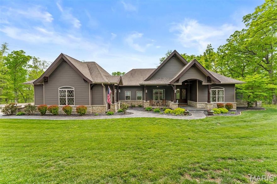 Discover unmatched luxury and versatility in this custom Craftsman-style estate, perfectly situated on a private, wooded 5-acre lot. From the moment you arrive, striking architectural lines and manicured landscaping set the tone for a home of exceptional quality and design. At the heart of the home, a magnificent open-concept great room seamlessly connects to the gourmet kitchen—ideal for both everyday living and entertaining. Natural light pours through expansive windows with custom draperies, flanking a floor-to-ceiling stone fireplace, creating a warm yet sophisticated ambiance. The kitchen is a true showpiece, featuring custom cabinetry, quartz countertops, stainless steel appliances including double wall ovens, a stylish subway tile backsplash, and an expansive center island with abundant storage—perfect for casual mornings or hosting on a grand scale. Retreat to the luxurious primary suite, a private sanctuary complete with a spa-inspired ensuite designed for relaxation and comfort. Step outside to a newly renovated deck, patio, and fire pit—perfect for entertaining or unwinding while taking in the unparalleled views and peaceful surroundings. The finished walk-out lower level expands the home’s living space with a secondary family room featuring a stone fireplace and custom built-ins, a media room with custom draperies, fourth bedroom, and full bath. Entertain with ease at the stunning custom bar, complete with professional-grade ice machine, custom cabinetry, and dishwasher. Additional highlights include a finished 3-car garage, a spacious laundry room with a mud sink, and high-end finishes throughout. Modern conveniences such as an irrigation system, Storm shelter/safe room with concrete lid, currently being used for root or wine cellar off the bar. Whether you're relaxing on the deck, hosting guests, or floating along Big Creek, this property offers a true everyday escape. Ideally located just 5 minutes from Troy and 15 minutes from Wentzville.
