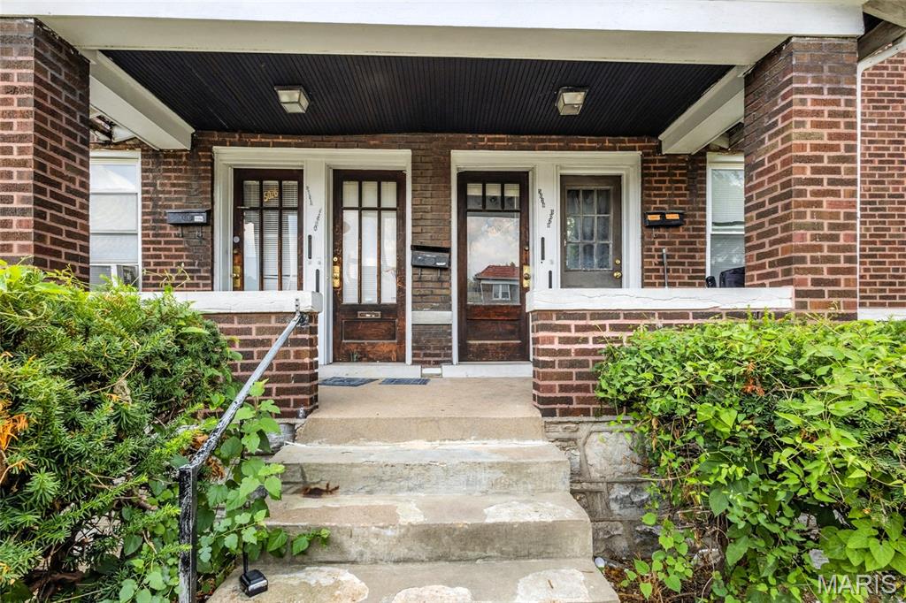 View of exterior entry featuring covered porch and brick siding