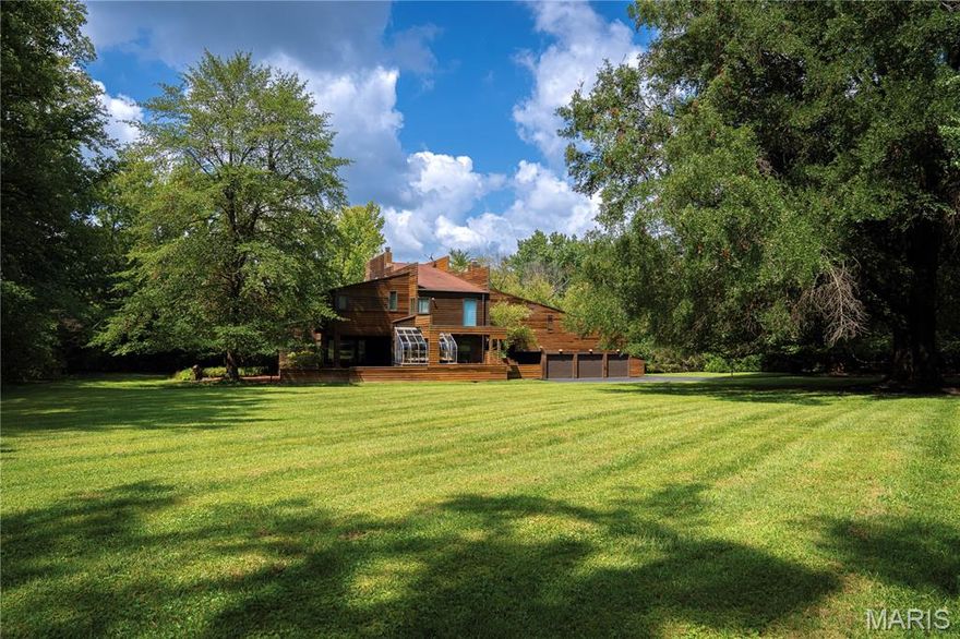 The Kohn House, a modernist masterwork designed by noted architect Carl Safe in 1974, is nestled into 2.38 private acres in one of Ladue’s most prestigious enclaves.  The three-level home clad in redwood siding boasts over 5,000 square feet of living space and embodies harmony between architecture and nature, combining timeless design with modern comfort. The initial turn up the long driveway provides a dramatic approach that reveals the quiet confidence of the residence — broad horizontal lines, organic materials, and sculptural geometry blending effortlessly into the landscape. Inside, a light-filled interior unfolds with an ease that feels both intimate and expansive.  The foyer offers a true signature of mid-century style — a sightline through the house to the verdant backyard — before turning to a living room that soars up two levels past a balcony and clerestory windows that bathe the sanctuary in soft, shifting light, creating a dynamic setting that feels alive with the rhythm of its environs. The space is perfect for entertaining, with a hidden wet bar, fireplace, and built-in seating beneath windows that impart views of the property’s lush surroundings.  The formal dining room is framed by windows on three sides, as well as multi-level redwood decks that extend the flow outdoors. Every room of the home was designed with at least two exposures, allowing light and greenery to animate the interiors throughout the day.  The main level also showcases an office with dual built-in desks, a family room that connects to an outdoor deck and greenhouse, a kitchen with double appliances and butcher block island, and an adjoining breakfast room with floor-to-ceiling windows and screened porch that’s perfect for al fresco dining. Two curved stairways lead to the second level, where the primary suite includes a skylit study, walk-in closet, and walk-through dressing areas with additional closets on either side of a tiled bath drenched in light from a skylight above.  Four more large bedrooms and two additional full baths — including one en suite — complete the upper level, with the ability to use one bedroom as a sitting room or secluded workspace. A hallmark of architect Carl Safe’s brilliance was to place courtyards in each corner of the house, allowing natural light and outdoor access that converts the lower level into an enormous additional living space, one that includes two huge recreation rooms, a full bath, laundry and storage rooms, and a soundproof music room with a wall of windows.  The largest courtyard features a fountain and outdoor seating, with a staircase that leads up to the entertainment spaces in the backyard. The property also highlights a tennis court, a porte-cochere that connects the house to a 3-car garage and its large loft, and an expansive parking area. Don’t miss out on this rare opportunity to own a modernist gem — available for the first time — in one of Ladue’s premier neighborhoods!