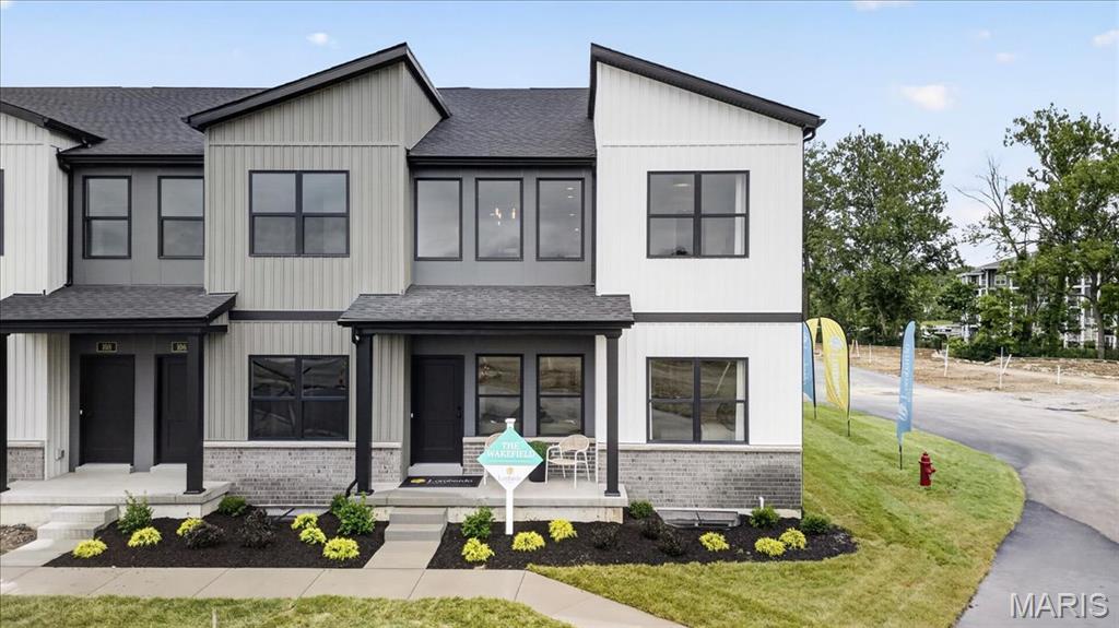 Modern townhome exterior featuring a contrasting facade of vertical plank siding and brick, a dark entry door, and manicured front landscaping
