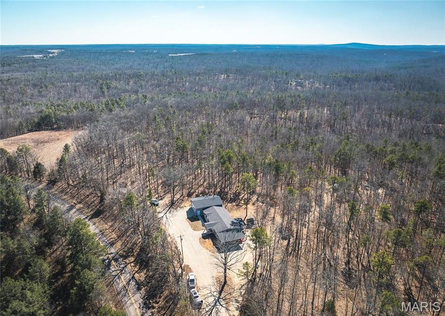 Welcome to your private country retreat—where modern comfort meets the outdoors. Built in 2023–2024, this spacious 4-bedroom, 2-bath manufactured home sits on 6 +/- beautifully wooded acres with direct access off paved State Highway HH, offering both convenience and seclusion. Whether you’re searching for a full-time residence, hunting basecamp, or weekend getaway, this property checks all the boxes.

Step inside to an open-concept layout designed for comfortable living and entertaining. The large kitchen features a center island perfect for gathering, a walk-in pantry for ample storage, and seamless flow into the dining and living areas. A cozy fireplace anchors the living space, creating a warm and inviting atmosphere year-round. The oversized master suite offers a peaceful retreat, complete with a spacious ensuite bath featuring a large walk-in shower.

Outdoor living is just as impressive. Enjoy your morning coffee or unwind in the evenings on the covered deck overlooking your wooded acreage. The land provides excellent hunting opportunities with abundant wildlife, made even better by bordering Missouri Conservation ground to the east and north—expanding your recreational access right out your back door.

Improvements include a 2-car carport, oversized attached garage with an all-concrete storm shelter/safe room for added peace of mind, and an oversized shipping container for additional storage of equipment, tools, or outdoor gear.

If you’ve been looking for newer construction, acreage, privacy, and direct access to exceptional hunting ground—this is a property you won’t want to miss. Additional acreage available for purchase as well.