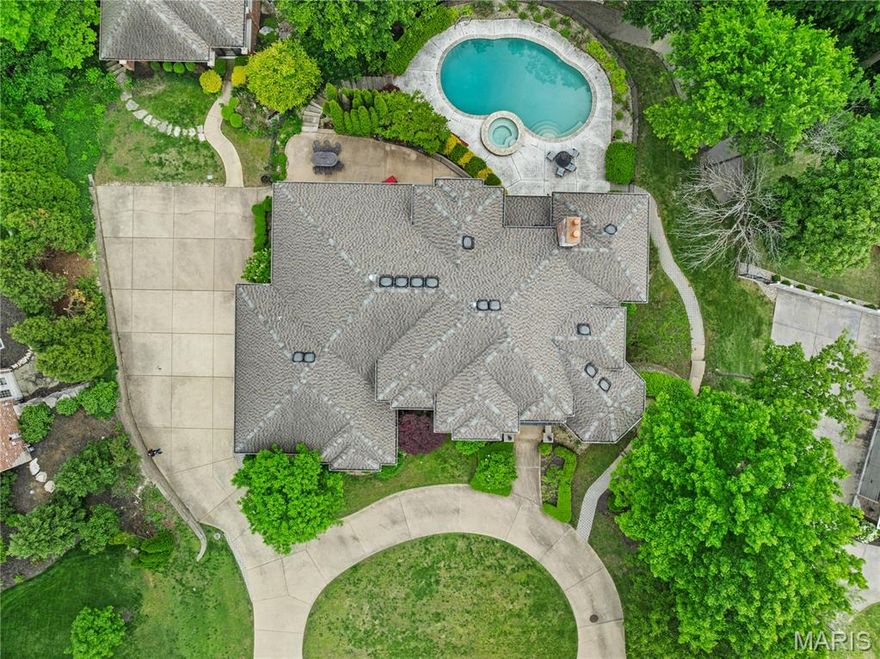 This impressive 6,000+-square-foot brick-and-limestone home is set on 1.29 acres in Sunset Hills and includes a separate 2,000+-square-foot, two-story guest house. The thoughtfully designed layout is ideal for both everyday living and entertaining. Hardwood floors flow through the living and dining areas into the kitchen. The kitchen offers generous cabinetry, extensive workspace, a large walk-in pantry, and a breakfast room open to the family room. The dramatic two-story living room features a two-sided fireplace shared with the family room, while a circular library creates a fun spot for reading or working. The main-level primary suite includes dual vanities, a soaking tub, a separate shower, and walk-in closets. Upstairs, a loft overlooks the foyer and leads to three bedrooms - one with an ensuite bath and two joined by a Jack-and-Jill bath. The walk-out lower level expands the living space with a family room featuring a fireplace, a bar area, a bedroom, and a full bath. The guest house offers exceptional flexibility, with a private apartment above featuring a full kitchen and bath, and a freshly painted wine cellar below with a barrel-vaulted ceiling. Outdoor amenities include a pool and spa, plus a lower, level yard with a swing set.