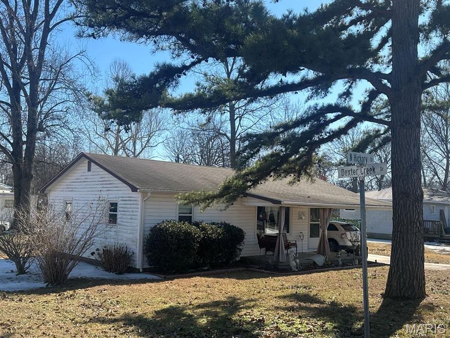 Charming and solid two-bedroom home on a corner lot with one full bath. The 1,014 sq. ft. layout features a living room, dining room, and kitchen with gas range, disposal, and dishwasher. A utility room includes a washer and dryer. Step through the nearly new patio door to a covered deck and fenced yard, great for pets or play. A storage building holds tools and lawn equipment. Inside, hardwood floors and roomy closets enhance both bedrooms. Comfort is provided by a natural gas wall furnace and two window A/C units. The hall bath offers a tub/shower and updated vanity. Additional highlights include a composition shingle roof, gutters, vinyl siding, covered front porch, and a concrete driveway leading to a carport—combining comfort, convenience, and classic appeal.