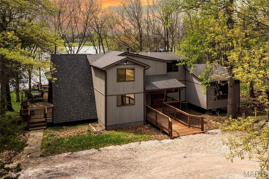 Welcome to 803 S Aspen Point Drive, a charming retreat nestled on the picturesque shore of Lake Aspen! With over 125’ of shoreline & grassy level lot, this reclusive retreat will have you feel worlds away while being just a short drive from the greater St. Louis area! This beautiful chalet offers a perfect blend of modern comfort & rustic charm! Inviting open floor plan featuring a spacious Living Room with vaulted ceilings & cozy stone fireplace, perfect for relaxing or entertaining. Kitchen is designed for both function & style, with sleek granite countertops, ample cabinetry & modern appliances—ideal for hosting family & friends. Main Level Primary Suite is a true oasis, offering a peaceful retreat with large windows that allow for stunning views. Outside finds expansive wrap-around deck, covered porch and firepit, ideal for enjoying the fresh air & natural beauty of the area. The wooded lot offers plenty of privacy, while still being just moments away from Innsbrook amenities!