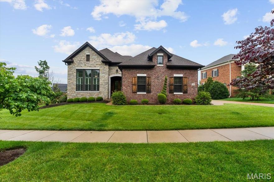 This impressive stone-front, brick home offers a blend of elegance and quality. You'll immediately notice the beautiful arched entry doors, high ceilings, hardwood flooring, custom moldings, and built-in details. The abundance of natural light and grand entertaining areas are truly inviting. The formal dining room, complete with striking pillars and an elegant chandelier, sets the stage for memorable gatherings. The two-story living room, with its cozy gas fireplace, seamlessly connects to a spacious eat-in kitchen. This culinary haven boasts a massive quartz double-edged island, chef-grade appliances, and ample storage. Off the kitchen, a three-season room offers the perfect transition to outdoor living. The main floor primary suite is a true retreat, featuring a tray ceiling, his-and-hers walk-in closets, and a spa-like ensuite bathroom. Upstairs, a landing area overlooks the living room and the lovely yard. You'll find two additional bedrooms, each with its own ensuite bath and walk-in closet. Downstairs provides additional living and entertaining space, including a bedroom with a walk-in closet and bathroom. A fireplace and wet bar add to the appeal, and a walk-out basement provides easy access to the backyard. Residents of this beautiful private gated community can enjoy leisurely strolls along the paths and peaceful moments by the reflecting pond and waterfall. Close proximity to Bellerive Country Club and a half mile from Whitfield School, this one is not to be missed!