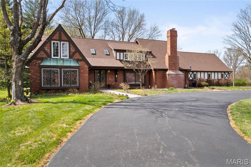 Filled w/classic details, this Tudor-style home will delight! Elegant front doors, reclaimed from an historic downtown building, invite you to enter this substantial home. Sunlight streams through the living room’s large leaded glass window. An even more spectacular stained glass window graces the primary bath. The great room w/ traditional boxed wood ceiling, detailed millwork, & fine English fireplace, will beckon your guests to sit for a cocktail & a chat. Expansive dining room has another elegant fireplace & adjacent brick sunroom-perfect for morning tea. Eat-in kitchen overlooking the backyard & opening to the dining room features high end appliances & abundant workspace. Lrg stamped backyard patio is surrounded by a level yard and quiet surroundings-so many possibilities! 1st floor primary suite includes spacious bathroom & private deck. 4 additional BRs & bonus room w/ vaulted ceiling complete the upstairs. 3car garage.The perfect home in the perfect neighborhood to make yours! Some Accessible Features