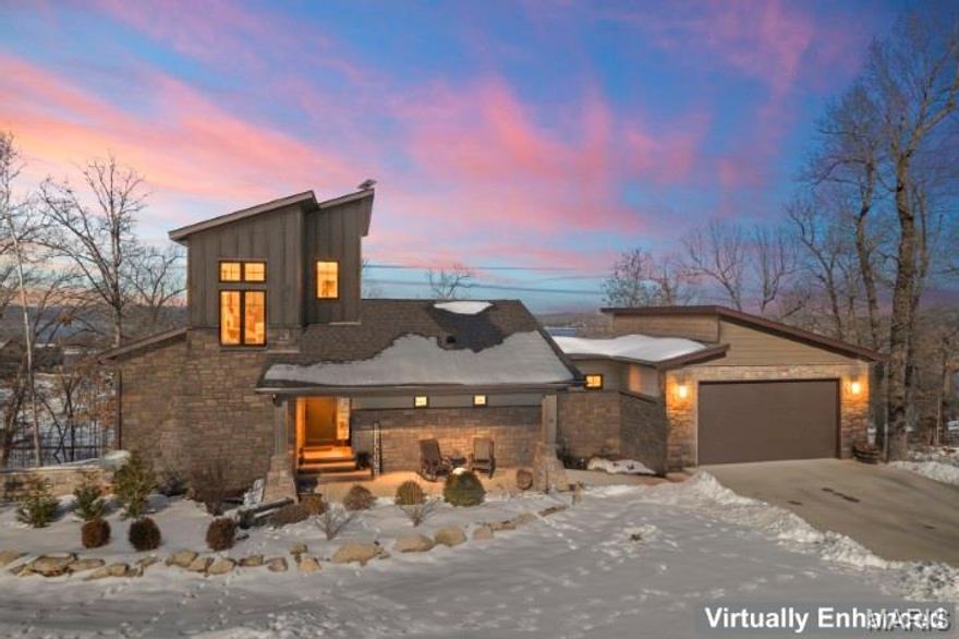 This contemporary lake home features a good winter lakeview, which becomes limited when the trees leaf out. Wood floors, a vaulted living room with a linear fireplace, oversized windows, and both covered and open decks with modern railings to include patio furniture and a hot tub. At the heart of the home, the kitchen becomes a natural gathering place. The expansive island draws everyone in—whether it’s morning coffee before heading to the water or shared meals after a full day at the lake. Thoughtfully designed with custom cabinetry, quartz surfaces, and a walk-in pantry, it balances beauty with everyday functionality, making hosting feel seamless. The main-level primary suite includes high ceilings, a spacious bath with double sinks, LED mirrors, quartz countertops, and a 4x7 walk-in shower, plus generous closet space with built-ins and washer/dryer hookup. The lower level offers a family room with gas fireplace and deck access, a second bedroom suite with soaking tub and walk-in shower, laundry room, and ample storage. There is a wet bar hook up stubbed in. Upstairs is a guest suite with a loft area. Two-car garage with potential for an additional workshop or garage with road access. Boat ramp located one mile down Hwy H. This is more than a lake home—it’s a place where time slows, connections deepen, and memories are made season after season.