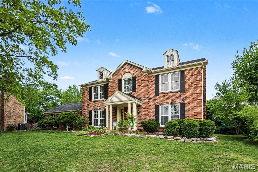 Traditional brick exterior featuring a covered porch with white columns, dormer windows, and black shutters