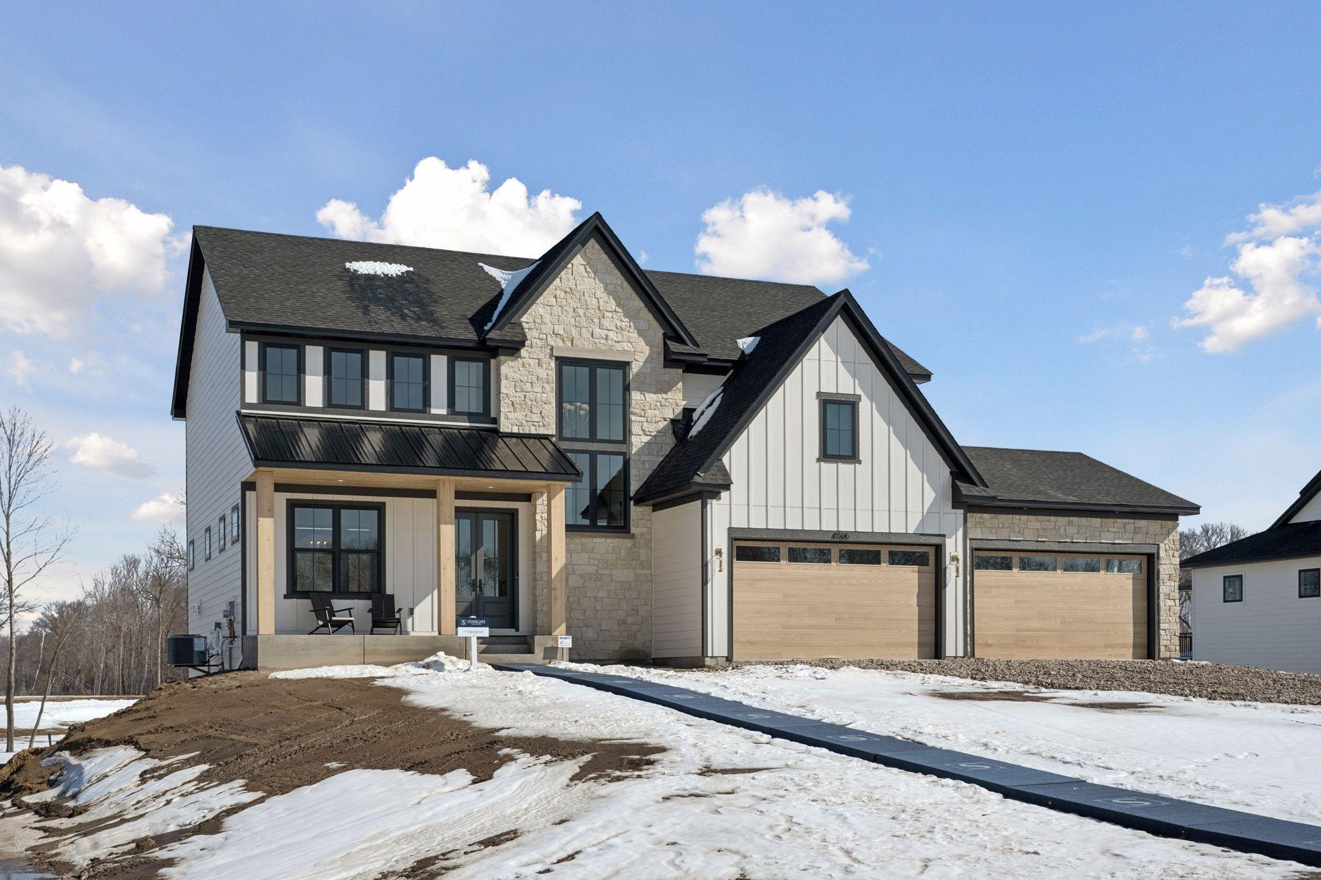 Front elevation rendering of Stonegate Builders' new Fremont Model in Elwell Farms! Stone and natural earthy toned exterior with ample space in the 4 car garage!