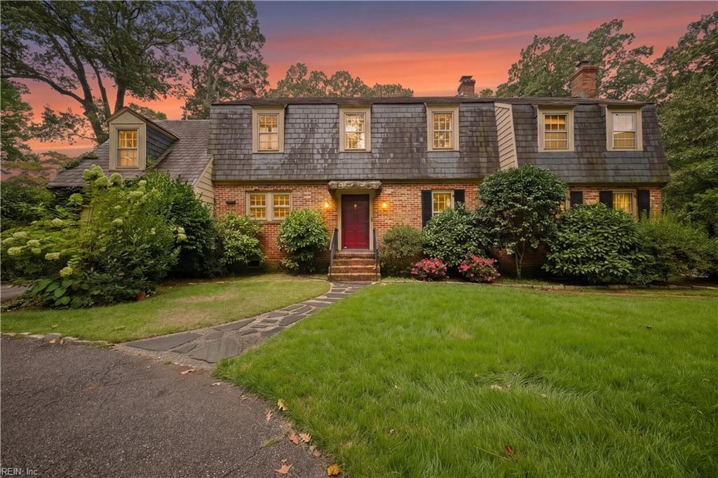 Brick house with a gray shingle upper story and red front door at dusk.