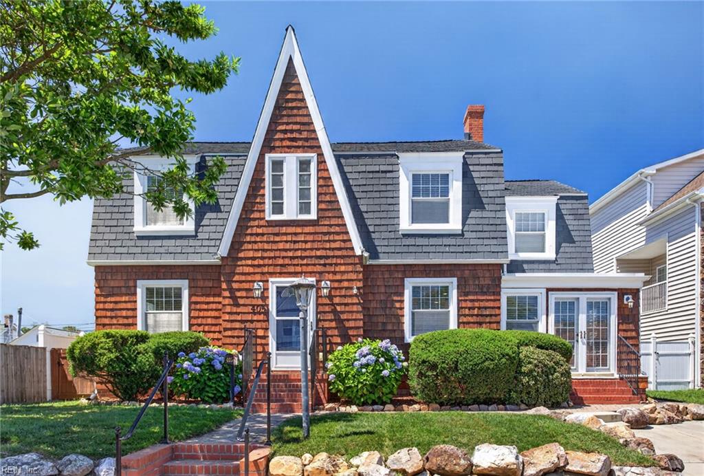Shingle-style house with a steep front gable, slate roof, hydrangeas, and stone landscaping.