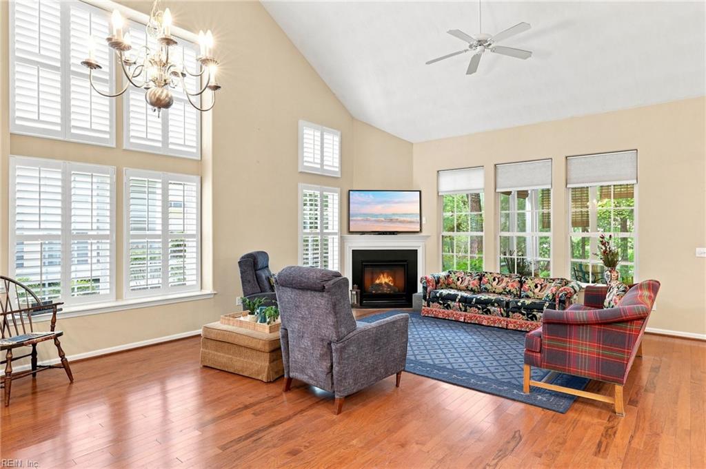 Furnished living room with vaulted ceiling, tall shuttered windows, hardwood floors, and a fireplace.