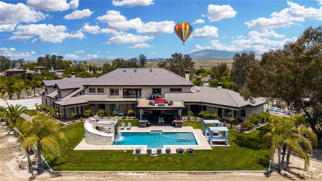 Nestled on a quiet cul-de-sac in the heart of Temecula Wine Country, this extraordinary estate offers nearly 8,500 square feet of luxurious living space on over 2 acres, with breathtaking views and world-class amenities. Just a quarter-mile from the first winery and a short drive to Old Town Temecula, this home provides the perfect blend of privacy and convenience. The well-designed floor plan features eight bedrooms and nine bathrooms, including four bedrooms on the first floor, two of which have en-suite bathrooms, plus a separate laundry room. The second floor boasts three additional en-suite bedrooms, along with an attached ADU offering private backyard access, its own one-car garage, a dedicated staircase, a full kitchen, a living area, a bedroom, a bathroom, and a separate laundry room with washer/dryer hookups. Also on the second floor is a spacious balcony with a built-in bar, offering stunning views of the wineries and backyard. A spiral staircase connects the balcony to the backyard for seamless indoor-outdoor living.
The third floor features a versatile bonus room or additional bedroom with a half bathroom, perfect for a private retreat or entertainment space.
Exquisite craftsmanship is showcased throughout, featuring a grand wrought-iron staircase, crown molding, and elegant flooring. The gourmet kitchen is a chef’s dream, equipped with high-end Thermador appliances, a built-in refrigerator, dual dishwashers, and custom cabinetry.
Designed for entertaining, the resort-style backyard is a paradise featuring a stunning pool with a waterfall, grotto, slide, and water features, plus a fully equipped outdoor kitchen with granite countertops, a pizza oven, BBQ, and more. The expansive six-car garage includes RV parking, a workshop area, an enclosed office or storage space, and a half bathroom. This exceptional estate is a must-see!