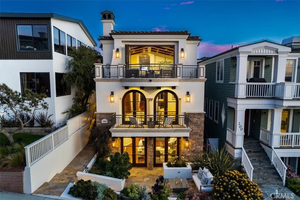 This timeless Santa Barbara style beauty is located within close proximity of Downtown Manhattan Beach and is just two blocks from The Strand along a gas lamp lined walk-street. Accordion doors frame up show-stopping views of the ocean and the Santa Monica mountains to the north from the open concept upper level living room. Gorgeous vaulted wood beam ceilings carry the classic California coastal design through the main entertaining areas. Step up into the expansive chef’s kitchen that centers around a massive island and flows effortlessly on into the more casual family room which enjoys south facing PV hill and ocean views.
The kitchen features a full suite of high end appliances from the GE Monogram series, to SubZero, Viking and Perlick. Warming drawers, a prep sink, dual dishwashers, Perlick freezer drawers and a custom pantry wall complete the ultimate functionality of this ideal workspace. Skylights flood the area with abundant natural light. The family room centers around a cozy fireplace while enjoying views of the ocean beyond, and there is a bonus built-in home office area as well as a guest powder room.
The primary bedroom suite is located on the main entry level of the home and enjoys a private fireplace and deck, as well as a luxury bath retreat with separate jetted soaking tub and walk-in shower. The laundry room is conveniently located on the same level as the main bedrooms. A 3-stop elevator can assist with delivery of bulk items and groceries throughout the entire home. Two additional bedroom suites are found on the main entry level and they share a joint balconette.
The beach level opens to a large walk-street patio off of the beach room which flows to the 5th bedroom (currently being used as a home office). A large wet bar is close at hand and is ideal for entertaining. A 3/4 bath and a private guest bedroom are also found on this level, along with direct access to the 3-car garage. Step right out from the beach level living area onto the walk-street and you’re within just a few blocks of world class surf as well as all the thriving community activity found in Downtown Manhattan Beach!