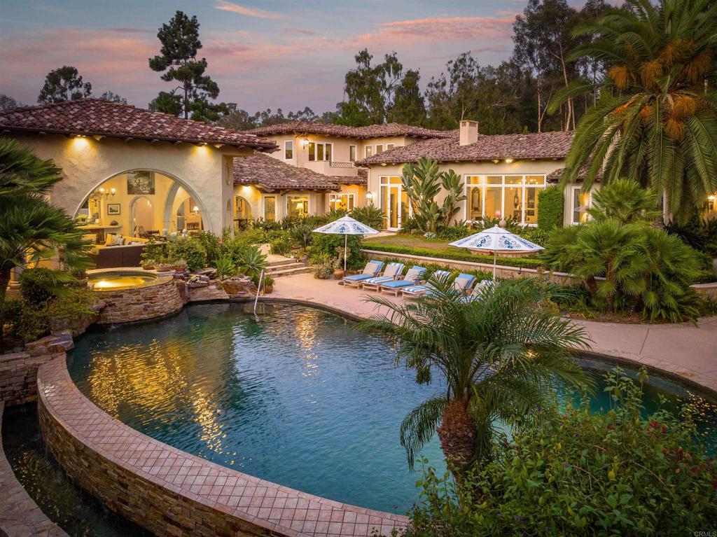 The sought-after and convenient West Side of Rancho Santa Fe’s exclusive Covenant provides an appropriately stunning setting for this bespoke estate, where four acres of mature and manicured grounds offer beauty at every turn. An environment of Timeless Elegance, expressed by David Easton (designer of the home), is enriched with indoor/outdoor living that is easily enjoyed year-round, given the San Diego climate, considered the best in the country. Six ensuite bedrooms, a regal office with rich wood paneling and fireplace and a luxurious detached guest cottage define the property. A magnificent primary wing features an oversized bedroom suite with sitting room, two massive walk-in closets, two bathrooms with a large steam shower, a massage room with sauna and an adjacent bedroom/gym. Gracious living areas encompass a sweeping staircase, temperatured wine storage, formal living and dining rooms, gallery-sized hallways, large game/bonus room and spacious family room with fully appointed bar, fireplace and casual dining. The professionally designed kitchen hosts the finest appliances, where everyday cooking becomes a celebration in the heart of the home. Relaxed, luxurious living continues throughout enchanting grounds that host an entertainment pavilion with living/dining room, full kitchen, an entertainment center, fireplace and half bath. Refresh in a vanishing-edge pool with waterfall and spa and explore park-like pathways, where a vegetable garden provides farm-to-table freshness. Discover flat, useable space for a future sport court or equestrian facilities (with RSF Association approval). The estate features an attached five-car garage, is connected to city sewer and is served by high-speed fiberoptic internet service from Race Communication, the leading internet provider in the United States. The community enjoys the benefits of a 24/7 private patrol, and is within close proximity to recreational facilities, world-class healthcare, and leading public and private schools, including the Roger Rowe K-8 School District. A Social Membership to the Rancho Santa Fe Golf Club is included, and well-maintained community sports fields and more than 60 miles of dedicated and groomed community riding and walking trails are enjoyed by all Covenant homeowners.