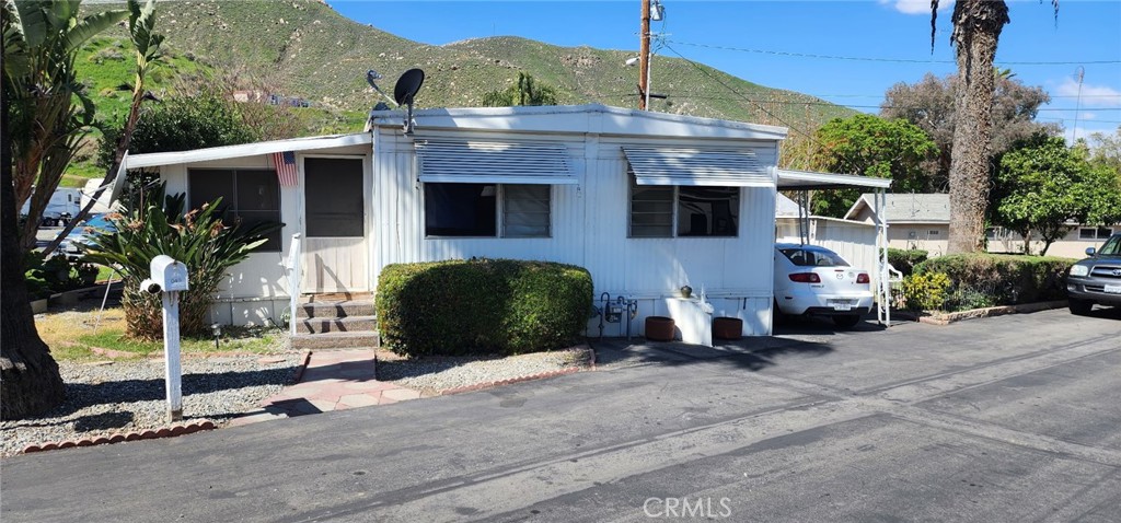 The home has an enclosed screen porch and a wheelchair lift. It is located on a corner lot with a small yard. There is also a shed for additional storage.