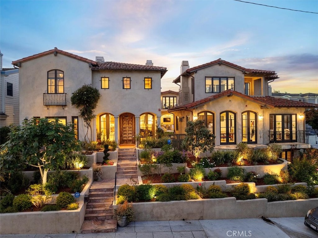 Why settle for ordinary when you can have extraordinary—on the high point of a beautiful tree-lined street, referred to as one of the best streets in the prestigious tree section of Manhattan Beach is a one-of-a-kind custom-built Spanish Colonial, a haven of luxury and sophistication with amenities that take daily living and entertaining to the next level.
At first glance, the prominent curb appeal displayed by architecture adorned by wrought iron details and lush-tiered landscape provides a private and serene backdrop. Beyond the stunning door the experience begins—the primary home is a masterpiece of design and functionality: open floor plan, cathedral ceilings, hand-cut travertine floors, and folding walls of glass doors allow sunlight to filter throughout the vast space—the main level comprised of a culinary enthusiast kitchen, dining area, living and family room, office/bedroom, and center courtyard w/fireplace for inviting alfresco dining and entertaining. The staircase beckons you to the upper-level open-air walkway separating the primary suite from other bedrooms for ultimate privacy. The dreamy suite exudes a romantic fireplace, bathroom w/dual sinks, walk-in shower, jetted tub and enormous walk-in closet. In addition, on this level are 4 comfortable bedrooms, 2 well-appointed baths w/dual sinks, playroom, laundry room w/dual washer and dryer and an abundance of storage.
Beyond the folding glass doors is the heart of this magnificent residence, a sparkling pool with waterfalls, spa, outdoor kitchen and bar. Just beyond the pool, a raised open-air colonnade with firepit creates a relaxing space and connects two separate dwellings. The guest retreat envelops family and friends in comfort, an open-concept design w/separate living area and fireplace, ensuite bedroom, and balcony offering lovely views. The entertainment wing offers a home theater, game room, fireplace, wine cellar, wet bar, and even 2 bedrooms w/3 baths for overnight guests. Love Where You Live