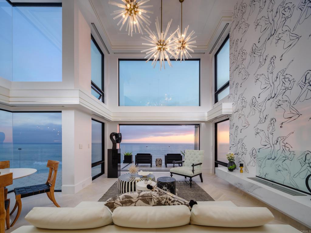 Stunning ocean-front three-story contemporary home features a unique collaboration between architectural and interior design by Tiffani Baumgart, a local San Diego designer, who created an experience like no other. It’s all in the details: this bespoke home was carefully thought out with custom high-quality elements that took years to gather from around the globe. Both the home and designer have been featured in: WSJ, Architectural Digest, Better Homes & Gardens, MyDomaine, Mansion Global and Modern Luxury. The achromatic color scheme offers tranquility with striking patterns and textures that uniquely adorn each room. The color scheme allows the dramatic focal points of the ocean and sunsets to be accentuated through every room of the house. The element of light is carefully layered into the design, from the movement of the sun, to the soothing glow from the dimmable lights that are controlled with a Lutron system. This smart home is easily controlled from anywhere in the world with your smart phone to construct any desired mood, where you can situate the lights, blinds, heat and jacuzzi. The SieMatic kitchen cabinets have an innovative use of space with a timeless style, which were custom designed by Baumgart. The Calcutta marble waterfall island has an inset Spekva brand wood slab detail at the four-person breakfast bar that is complimented by the Lindsey Adelman light fixture, Miele and La Cornue appliances and imported Swedish tile backsplash. The jewel of the dining nook is a pendant by Lindsey Adelman, and the star burst Hanley chandeliers in the two-story ceiling of the living room by Arteriors, which is also a focal point from the primary bedroom. The primary suite is designed to capture direct ocean views from the private second story loft-style room with a large bathroom with steam shower, vessel tub, private water closet with bidet, dual sinks, a large custom walk-in closet with custom built-in cabinets and shelving. The lower level features the a large private jacuzzi with an imported tile surround, a lounge area with an imported French hammered tin ceiling and French antique door wainscoting. This double lot has a vast outdoor living space with the expansive multi-level decks and courtyard, which allow a true indoor-outdoor experience from each living area, especially when the frameless folding Cover Glass doors slide open. The courtyard by the front of the home is a welcoming entry home with a custom crystal water feature, custom horizontal light wall and landscaping. The energy efficient home has 33 owned solar panels, tankless hot water heater, whole home radiant heat and in-floor radiant in each bathroom. Three blocks to iconic Carlsbad Village, which is the downtown commercial area of Carlsbad and is a center for arts, culture, shopping and dining.
