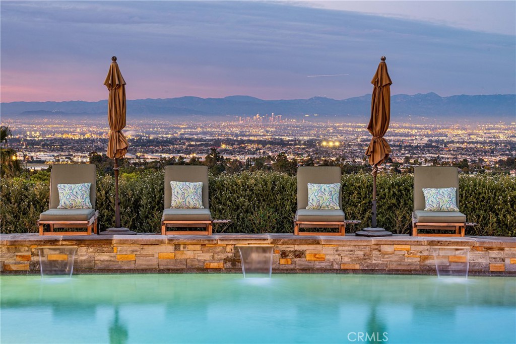 Luxurious country living, Incomparable views, Endless amenities!
A long, private drive leads you past a vineyard, lavender garden and fruit trees to unobstructed views from the Queen’s Necklace to the Gerald Desmond Bridge on this gorgeous equestrian estate!
This 4475 sq. ft. Rolling Hills ranch was designed to take in the panoramic mountains and city lights from every room. Beautifully updated with high quality craftsmanship and impeccable taste. The gourmet chef’s kitchen features beautiful tile work that carries into all 7 bathrooms. Vaulted ceilings and large, plentiful skylights allow natural light to fill the open concept kitchen, dining and living areas. Two sets of tri-fold La Cantina doors open the living areas up to a 400 square foot covered patio with a built in outdoor kitchen that overlooks the pool, spa and fire pit for versatile indoor/outdoor living and entertaining. All 5 bedrooms include spacious ensuite bathrooms. The stunning master suite includes a cozy fireplace, walk-in closet, attached office and relaxing, spa-like bathroom. Off of the main house is a spacious, fully equipped 625 sq. ft. guest house with a large porch and its own private outdoor space. Nestled in the mature landscaping is a 2300 sq. ft. barn with a comfortable saloon, riding arena and lots of turnout spaces. A huge workshop with high ceilings and gardening shed and chicken coop add even more functionality to a property that has it all!