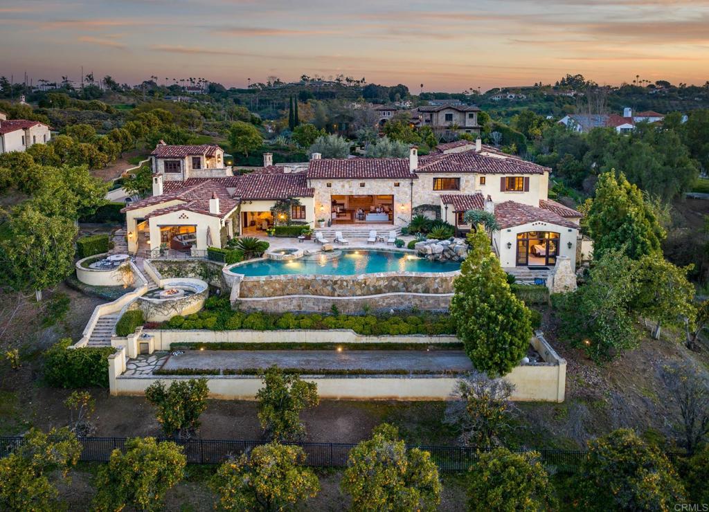 Exclusive luxury living has ascended to a lofty new pinnacle at this stunning custom residence in The Bridges, Rancho Santa Fe’s most enviable guard-gated resort enclave. Overlooking the 13th and 14th holes of the community’s gorgeous golf course, the sprawling estate impresses at every turn. Beyond a gated courtyard, the residence welcomes everyone with an open great room that showcases a towering open-beam ceiling, panoramic views and a wall of disappearing glass pocket doors. Five bedrooms and five full and three half baths in approximately 9,866 square feet provide privacy and personal comfort, with an expanded guest house reserved for pampering guests. A fireplace-warmed patio with spa joins a five-star primary suite, and a wood-paneled executive-caliber office, formal dining room, 1,500-bottle wine cellar, secondary office, and recently upgraded home theater make living the Good Life even better. High-end style and premium function unite in the kitchen, where custom cabinetry, dual breakfast nooks, a walk-in pantry with wine refrigerator, and Bosch, Viking, Miele and Sub-Zero appliances cater to every task. Nearly 1.97 acres, the rare, elevated cul-de-sac homesite offers sweeping canyon and golf views, a pool, spa and an outdoor loggia with kitchen and pizza oven.