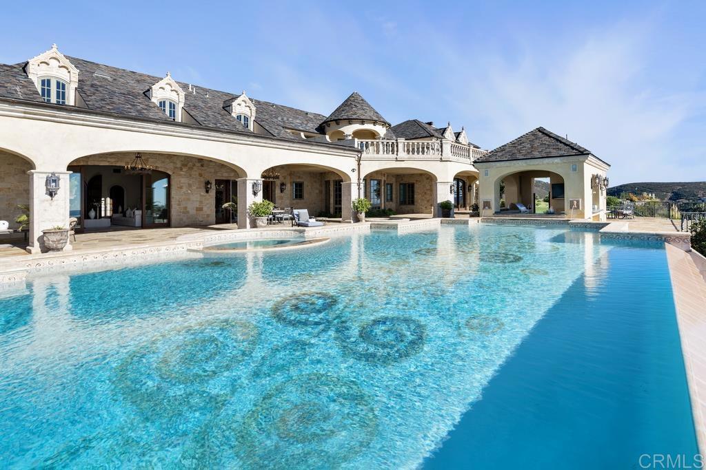 This masterfully built French Chateau-inspired estate is proudly perched on a private 4-acre site in the exclusive community of Cielo with panoramic views of the ocean, downtown skyline, and majestic mountains. Spanning 12,000 sq ft the spectacular estate showcases impeccable craftsmanship and architectural authenticity. Exquisite design in the fixtures and extravagant treatments, all with comfort and pleasure in mind are down each grand hallway and behind every door. The chef's inspired kitchen is a culinary masterpiece adjoining the great room with a massive 20' high stone fireplace and 24' ceilings. With a movie theatre, full wet bar, billiard gaming room, and subterranean wine cellar with tasting room, this home offers exceptional entertainment. Outdoor amenities include a covered loggia, resort-style pool with swim-up bar and fire features, elevated spa, built-in barbecue, stone firepit, fully equipped outdoor kitchen, ponds with water lilies, fragrant rose garden, 5-hole golf course with viewing deck, 11-car garage with generous motor court and a private 1,200 sq ft detached guest house. Energy-efficient with 100% Solar power. Every detail of extraordinary quality is exemplified in this stately residence. The 24-hour guard-gated community of Cielo offers many association amenities to include a community center, gym, clubhouse, tennis and pickleball courts, playgrounds, multiple pools, and basketball courts.