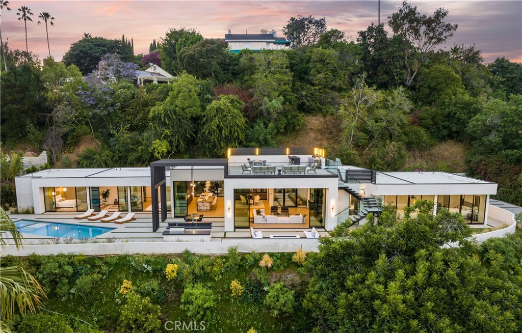 Modern architectural masterpiece boasting awe-inspiring views! This single-story home is an entertainer's paradise, complete with a private yard and a rooftop view deck. Situated high above iconic Sunset Boulevard, anticipation builds as you pass through elegant wrought iron gates and make your way up the secluded driveway. Step inside through the grand glass front door and be welcomed by an expansive great room adorned with floor-to-ceiling windows, revealing breathtaking city vistas. Effortlessly flowing, this space seamlessly connects the generously sized living room, perfect for cozy evenings by the fireplace, with the open kitchen featuring top-of-the-line Miele appliances, an elongated island for casual seating, and a separate prep kitchen for hosting delightful dinner parties in the spacious dining area. The epitome of indoor/outdoor living awaits as you open the glass walls, transforming the ambiance into a luxurious resort-like setting, complete with fire pits, fountains, a pool, spa, and multiple inviting seating areas. Ascend to the rooftop view patio, where you'll discover a second BBQ, a bar, and an additional seating area, all while being captivated by the unending views of the city and the ocean. The master wing of this estate offers a sumptuously appointed master bedroom, featuring a captivating wood accent wall, a custom fireplace, and a modern spa-inspired master bath complete with a freestanding tub and a multi-person walk-in shower. The adjoining room can serve as a bedroom, gym, office, or nursery, or alternatively, be transformed into an expansive walk-in closet with an additional bathroom exclusively for the master suite. The guest wing boasts wrap-around lighting, leading to two beautifully designed bedroom suites. Embrace the rich Hollywood history of this Bel Air site, once home to Joanne Carson and Truman Capote, as you create your own unforgettable memories in this bespoke estate meticulously crafted with attention to detail and featuring designer-selected finishes.