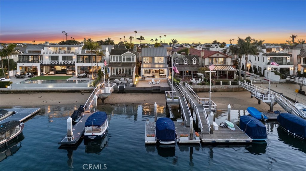 Enjoy twinkling city lights and panoramic Newport Harbor views from one of the preeminent addresses on the bay front – exclusive East Bay Avenue within the charming enclave of Peninsula Point. Exquisitely redesigned with a “to the studs” remodel, this on-point 4BR/4.5BA bay front residence was thoughtfully reimagined to check all of the boxes. With an open-concept layout, well-proportioned room sizes, and bespoke designer finishes, this harbor front home is easy to love. Stepping through the Dutch door entry you are greeted by coastal breezes and an inviting sense of home. The open living and dining areas are highlighted by finely crafted built-ins, state-of-the-art AV equipment, a cozy fireplace, and walls of glass that open to a covered and heated bay front patio and sandy beach that adjoin the private pier and dock. The professional-grade island kitchen is highlighted by a Majestic range, Sub-Zero and Bosch appliances, abundant storage and a separate walk-in pantry. An en-suite bed and bath are also conveniently located on the first floor of the home. Upstairs the primary suite with private terrace and expansive water views is designed for relaxation. Soft neutral tones and luxurious textures create a calming ambiance, while the spa-inspired ensuite bath features a deep soaking tub, rainfall shower, and dual vanity. Two additional guest bedrooms and baths have been finely curated with hand-selected finishes and welcome guests with comfort and style. The entertainment enthusiast will enjoy the stylish upper level media retreat. Here rich textures, moody lighting and culled nautical touches create a cinematic atmosphere at home. Enhanced by disappearing custom Murphy beds, this dramatic space also easily accommodates visiting family and friend over-flow. Additional amenities include an attached two car garage with adjacent third car parking pad, upstairs laundry room, beach shower, tailor-made garage built-ins, whole-house water conditioning, and exterior gas lanterns. Sited on one of the most scenic parts of the harbor this turn-key home is a remarkable opportunity in the very best of bay front locations. From sunrise coffee on your private dock to sunset wine with friends back at the house after a Duffy ride get ready to enjoy life on the harbor!