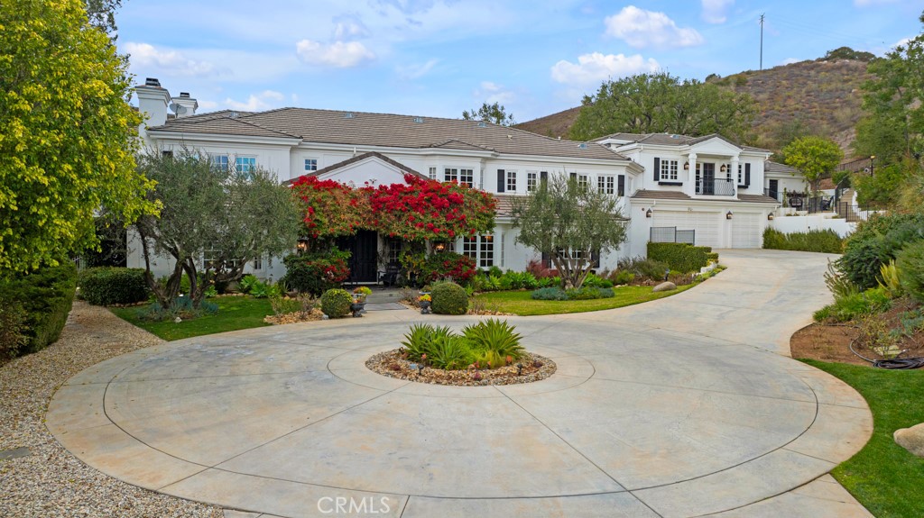 Nestled w/in prestigious North Ranch neighborhood of Westlake Village, this privately gated estate is a true masterpiece, offering over 2.3 acres of sprawling, picturesque grounds w/sweeping mountain views. Stately drive leads to grand turnaround & finished 3-car garage, hinting at the elegance that awaits inside. Double front doors open to breathtaking foyer w/soaring ceilings, curved front staircase & Versailles pattern limestone floors. The open floor plan showcases high-end finishes throughout, including rich hardwood floors, crown molding, decorative ceilings, wainscotting, custom window treatments, & recessed lighting. The main level features a number of rooms with versatile use, including a library/office with fireplace, lounge/zen room, and a formal dining room. Grand step-down living room boasts fireplace, two-story ceilings, full wet bar, & French doors outside. Gourmet kitchen dazzles w/Carrera marble counters, mosaic backsplash, central island w/auxiliary sink, breakfast bar seating, 2 walk-in pantries, & adjacent, sunny breakfast room. Spacious family room could also be first-floor bedroom w/walk-in closet & access to 2 powder rooms offering convenience & flexibility. Upstairs, luxurious primary suite is private retreat w/fireplace, sitting area, enormous walk-in closet w/skylights, & opulent en-suite bath w/steam shower, jetted tub, double-sink vanity, & marble floors w/inlay mosaic tile. Down the hall, 3 more bedrooms each offer walk-in closets & access to well-appointed baths. Secondary staircase leads to a private guest suite w/en-suite bath & large music studio/bonus room—perfect as a home office, gym, or studio—complete w/powder bath & separate entry. Additional features include a dedicated laundry room w/secondary fridge, 3 AC units, & media closet for seamless home entertainment. The estate’s breathtaking grounds are an entertainer’s dream, w/a grotto-style pool, spa, & cascading waterfall, covered patio w/speakers, heaters, & TV, walking paths, outdoor kitchen w/BBQ, sink, & wine fridge. Separate detached temp-controlled wine room w/brick flooring & custom racks. Lush landscaping includes a bounty of fruit trees—six types of citrus & avocados—along w/charming overlook spots, decorative yard art, & water features. Beyond the fenced yard, a nearly flat pad presents space for tennis court, guest house, additional garages. This is a once-in-a-lifetime opportunity to own a truly exceptional estate—don’t miss your chance to call it home!