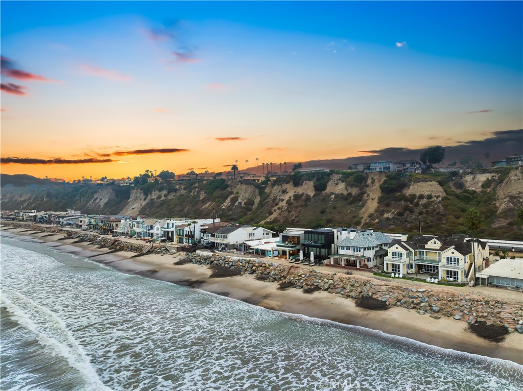 Standing directly on the sand along Capistrano Beach's exclusive guard-gated Beach Road community in
Dana Point, this extraordinary custom home pairs stunning modern architecture with panoramic ocean,
beach, Catalina Island, sunset, whitewater and coastline views. Natural wood, patinated copper, glass, metal
and concrete combine to distinguish exterior architecture that is destined to stand the test of time. Designed
by Mark Singer and built by Crawford Custom Homes with an interior by Terry Hunziker, the spacious, open
and light two-story residence is truly a seaside oasis that showcases a soaring double-height entry, open-
concept living spaces, and a bespoke selection of top-tier finishes and fixtures throughout approximately
3,503 square feet. Five bedrooms and five baths include four luxurious ensuites and a main-level bedroom
that is perfect for guests. Opening via a wall of Arcadia glass doors to a covered beachfront patio with spa
and built-in BBQ, the living room, dining room and kitchen form one seamless space that generously
accommodates impressive entertaining and easy daily living. A custom entertainment wall with linear
fireplace and surround sound anchors the living room, and the kitchen displays a large island with seating,
sleek European-style frameless cabinetry, open shelving, leathered quartzite countertops, and a custom
backsplash with built-in storage and a unique in-wall spice organizer. Chefs of every skill level will benefit
from top-of-the-line appliances that include a built-in cabinet-matched Miele refrigerator, built-in ice-maker,
and a drawer microwave and versatile multi-burner cooktop from Gaggenau. Ascend a dramatic floating
staircase to the second level of this peerless beachfront home, where floor-to-ceiling windows welcome
natural light, and a lavish primary suite overlooks the sand, breaking waves and Pacific Ocean while
revealing a deck, freestanding tub, separate shower, floating vanities, and a walk-in closet with custom built-
in cabinets. Concrete walls, wood-plank ceilings, chic lighting and custom built-ins are featured in select
areas, and radiant-heat flooring, Crestron home automation, a two-car garage, three parking spaces and
storage across the street, and a built-in back-up generator elevate preferred living. Residents of Beach Road
enjoy a private beach extending nearly 1.5 miles that is close to Dana Point’s harbor and Lantern District, and biking, hiking and walking trails.