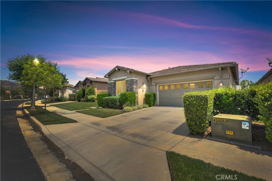 A Must See sparkling GEM with fabulous city light and mountain views from oversized yard with custom designed patio and landscaping. This home is located in a premier Trilogy at Glen Ivy 55+ gated golf resort like community surrounded by the Ted Robinson designed public golf course. The Satsuma model has 1,966 sq ft of living space. Newer AC system and newer installed water filtration system! Custom paint, plantation shutters and large crown moldings. Office/den/Flex room possible 3rd bedroom. Model has formal living, dining room, focal fireplace in family room, media center, ceiling fan and large windows framing that panoramic view. Gourmet kitchen featuring granite counters, island with sink, dishwasher and counter seating with pendent lights, stainless steel range, microwave, cabinets with roll-outs, pantry, built-in desk/ tech center plus a separate kitchen dining area with a sliding door to the integrated covered patio. The Primary suite has a ceiling fan and slider to the patio with endless views. Elegant primary bath with granite dual sink vanity, custom tiled shower, dual medicine cabinets, linen cabinet, ceiling fan and walk-in closet with mirrored closet doors and closet organizers. The guest suite has mirrored wardrobe doors, ceiling fan and adjoining full bath with granite vanity and tub and shower. Interior laundry room. HOA dues include front yard maintenance. Trilogy has a grand ballroom for community events, billiard room, craft studio, learning center and meeting room, card rooms. The Blue Water Sports Club features an indoor pool with running/walking track above with views of the Cleveland National Forest, state-of-the art fitness center, indoor/outdoor pool, outdoor large spa plus two tennis courts, pickleball courts, horseshoes, bocce ball, shuffle board and many club activities.