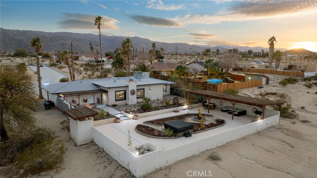 Welcome to Two Mile Road, where adventure meets style in the heart of the high desert. Just seven miles from Joshua Tree National Park, this 3 bedroom, 2 bath custom-designed home sits on over 6 acres of breathtaking desert landscape, offering privacy, serenity, and endless possibilities. Currently operating as a successful short-term rental, this property is ready to continue generating income or become your own private oasis. A long driveway leads to a two-car garage and abundant open space, perfect for storing recreational toys. The gated front courtyard provides a private outdoor sanctuary, setting the tone for the unique features inside. Spanning nearly 1,900 sqft, the home is designed with LVP flooring, wood panel ceilings, and captivating desert views from the moment you walk in. The open-concept layout includes a dining area with sliding glass doors to the courtyard and an upgraded kitchen featuring granite countertops, a stylish tile backsplash, white cabinetry with pull-outs, stainless steel appliances, recessed lighting, and dual eat-up bars. An additional dining space is highlighted by picture windows offering unobstructed views of the vast landscape. The spacious living room boasts cathedral wood-beamed ceilings, creating a cozy yet expansive atmosphere. Down the hall, two secondary bedrooms showcase stunning views and share an upgraded bath with a walk-in shower and custom tile work. The primary suite is a tranquil retreat with breathtaking scenery and an en-suite bath featuring tiled floors, ample counter space, blue cabinetry, and a walk-in shower. The fully fenced entertainer’s backyard is thoughtfully landscaped with extensive concrete patio space, an above-ground spa, and ample room to expand. The property is on septic, fully electric with an optional gas hookup, newer roof, brand-new AC unit with optional Evaporative Cooling, and has the potential for an additional dwelling unit (ADU) or guest home. Don't miss this rare opportunity to own a desert escape with income potential in one of the most sought-after locations near Joshua Tree!