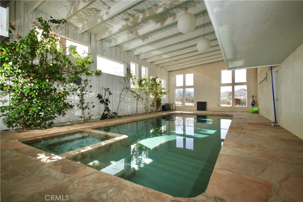 Your resort vacation home awaits. This home is stunning! With 3 bedrooms, 4 bathrooms as well as additional living areas, Oh, and did I mention the indoor solar heated, salt water swimming pool and spa? This home has been family owned from its creation. Split level design for separate spaces for endless options. Create your own private sanctuary or have endless entertaining possibilities. The flow and separate areas will allow for both private and resort style living. This home sits on 2.5 acres. Property is mostly flat and usable, with majestic Joshua Trees as well as other indigenous vegetation. Home has its own private well with Pelican full house filtration system, and an additional well which provides water for the pool and plants. Many well thought-out updates have taken place so the home is move in ready for yourself, and or guests. Updates include; individual mini splits in each bedroom, fresh exterior paint on the eves and fresh fog coat on the house with a fresh scrub/stucco on the exterior retaining walls. Snow coat on roofs 6 years ago with a touch up 1 month ago. New window screens, latches, and glass door locks. A complete remodel of the lower level which adjoins the swimming pool, makes it fully functional for social gatherings and or retreats. Exterior features include an attached 2 car garage as well as additional rustic outbuildings. Bring your horses and toys, the space is here. Plenty of BLM land nearby.
This home is in an ideal location, close to town, yet up the South Side of the Valley for enhanced views and privacy. 30 minutes to Palm Springs, 15 minutes to Joshua Tree National Park, as well as Pioneertown, and fantastic surrounding areas to enhance your desert lifestyle. Buyer, please check with the Town of Yucca Valley to see if this property will qualify for a retreat center or a special use facility for those seeking for a magical desert venue. An additional 5 acres(which also includes an additional private well) is available at an additional discounted price if the lucky buyers of this home choose to expand. Call today for further information or a personal viewing.
