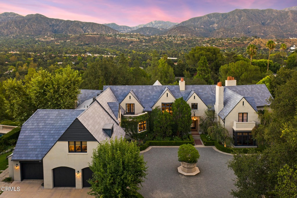 An architectural gem in the classic English Revival style, custom-built in 2001 on 1.8 acres of property featuring lush landscaping and spectacular mountain views, this majestic, private compound delivers a gracious lifestyle where leisure meets adventure. Bask in poolside splendor amid tranquil San Gabriel Mountain vistas, perfect your shot in pickleball or basketball, practice your swing in the batting cage or explore surrounding gardens and trails. Follow the gated, private drive to the hedged gravel motor court and enter via the foyer filled with an abundance of natural light. Most rooms boast dual views and all ground floor spaces offer access to outdoor areas perfect for entertaining. Verdant lawns, gardens, and brick patios with fountains and seating areas await intimate dinners or grand parties. Every detail is meticulously curated, from the hand-troweled plaster walls, dark ebony stained wood floors and artisan stonework, to the timeless handcrafted materials, custom woodwork, and European-imported tile. Relax in the expansive living room or the adjacent mahogany walled library with coffered ceiling, both featuring wood-burning fireplaces. With crystal chandelier and elegant sconces, the sun-kissed dining room and adjacent butler's pantry set the stage for your next soiree. A chef's paradise, the striking kitchen features Viking appliances, farmhouse sink, expansive marble island, and limestone counters. The family room wows with hand-hewn ceiling beams, wide-plank floors, an enormous stone fireplace, and French doors leading to a loggia with commanding archways framing pool and mountain views and an inviting outdoor fireplace. A three-car garage, two powder rooms and mud/laundry room complete the ground level. The spacious primary suite stuns with private terraces, intimate sitting room, dual closets, and spa-like bathroom with limestone floors, polished marble counters, nickel fixtures, and mirrored cabinets. The upper level also features four additional bedrooms with walk- in closets, laundry room, craft room/office with private terrace, reading nooks and plentiful storage. At the lower level, discover a billiard/media room with copper-topped mahogany bar and 900-bottle wine cellar, bathroom with steam shower, and home gym that opens to the pool area. Hosting is a delight in the outdoor kitchen with refrigerator and wood-burning pizza oven, surrounded by manicured gardens and mature fruit trees.