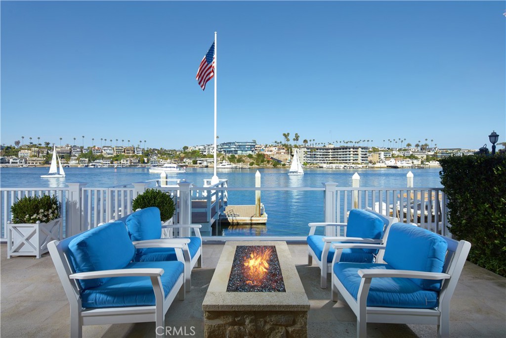 The pinnacle of Newport Beach living awaits at this picture-perfect bayfront home on the southern tip of the Balboa Peninsula. Offering 53' of frontage on the water and a private dock that can accommodate a vessel up to 45', this luxurious New England Coastal-style residence by Patterson Custom Homes impresses with panoramic channel views that encompass evening lights reflecting on the water, China Cove Beach in Corona del Mar, and Newport Bay’s access to the Pacific Ocean. Magnificent vistas can be enjoyed from both levels of the home and its rooftop, where 360-degree views can be savored from a bubbling spa. Spanning approximately 6,164 square feet, the shingled design impresses at first sight with stone accents, a slate roof, and a private, gated front patio featuring a welcoming Dutch entry door. A two-story foyer with a sweeping curved staircase opens to an interior adorned with handsome wood flooring, elegant custom millwork including crown molding and wainscoting, coffered ceilings, and exquisite hardware, fixtures, and handcrafted finishes. Five en-suite bedrooms and five-and-one-half baths include a main-level suite, and a bay-view primary suite with a fireplace and vaulted and beamed ceiling. A loft, custom home office, and bonus room/optional sixth bedroom offer versatility throughout. Entertaining is easy in a massive great room that opens to a large deck overlooking the bay and features a walk-in wet bar, fireplace, and direct access to a large fireplace-warmed dining room. The kitchen flows effortlessly to the great room and dining room, styled with features reserved for today's finest residences, including a grand island with bar seating and farmhouse sink, marble countertops, a full backsplash, butler’s pantry with utility sink, custom white cabinetry, built-in flush-mount Samsung TV, and top-of-the-line appliances like a built-in Miele coffee station, six-burner Wolf range with two ovens, a separate Wolf oven, warming drawer, and Sub-Zero beverage cooler.