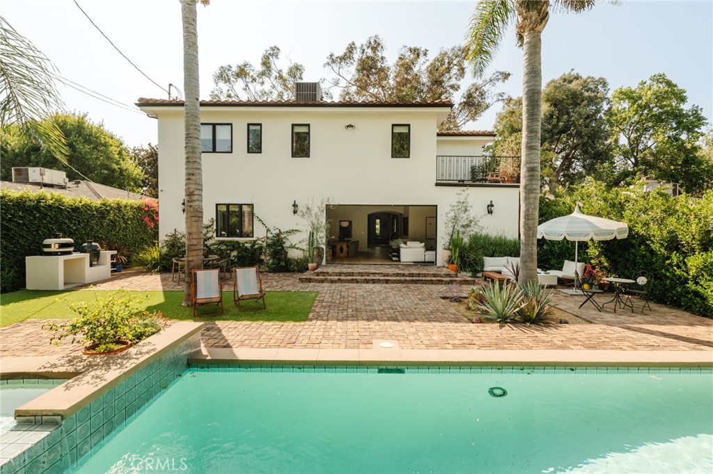 Tucked away in a prime Sherman Oaks neighborhood, this contemporary Mediterranean estate has been fully updated, blending sophisticated designer finishes with unique and personal touches. Designed by notable Architectural Digest Top 100 interior designer, Mandy Cheng, this property is a statement.
Upon entering, you’re greeted by double doors that lead into a grand foyer with soaring double-height ceilings, setting the tone for the home’s spacious and inviting atmosphere. One of the home’s standout features is the formal living space/library room, designed to offer a peaceful escape. It houses custom-built shelves and nooks for reading, making it the perfect space for relaxation and creativity.
The open-concept main living space includes a family room with a sleek fireplace surrounded by custom built-ins, stunning warm colors, a beautiful chef’s kitchen outfitted with top-of-the-line Viking appliances, and both formal and informal dining areas perfect for hosting family and friends. With floor-to-ceiling glass doors that pocket, this creates the perfect indoor-outdoor entertainment space, flowing into your nearly 8,000 square foot lush backyard. The first floor also includes a laundry room, a bedroom, a full bathroom, and a powder room. Upstairs, you’ll find two luxurious primary suites. The larger of the two features an intimate fireplace, private balcony, spacious walk-in closet, and a spa-like bathroom complete with a soaking tub, rainfall shower system, and double vanity. Additionally, two generously sized bedrooms with custom closets offer ample space for family or guests.