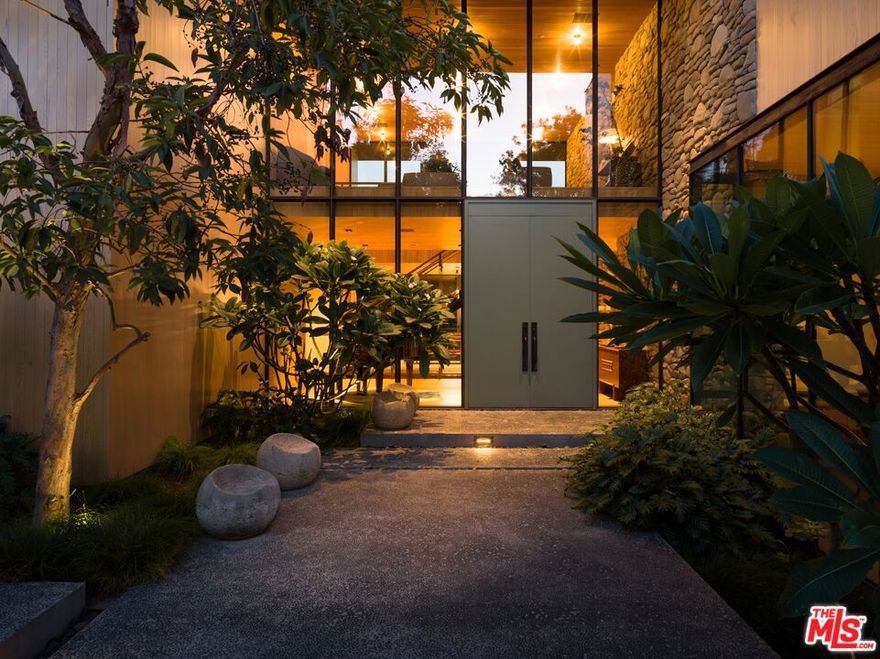 Presenting a one-of-a-kind, warm modern estate nestled in the exclusive enclave of the Riviera. Designed by renowned architect Bruce Bolander, with interiors thoughtfully curated by Studio Shamshiri, this bespoke residence spans just under 10,000 square feet and emphasizes natural materials that create a serene, inviting atmosphere throughout. The home features stunning 18-inch Dinesen wood flooring, renowned for its rich, organic warmth, and walls crafted from locally sourced Malibu stone, adding both texture and timeless elegance to the space. Disappearing glass walls and expansive skylights flood the interior with natural light, effortlessly blending the indoors with the lush outdoor surroundings. Outside, the resort-style backyard is an oasis of tranquility, featuring a sleek pool, a spa, and a spacious deck. The home also offers a seamless flow with a luxurious primary suite, complete with a private balcony, and beautifully appointed guest suites. The expansive basement includes an entertaining area, a fully equipped gym with a ballet barre, a steam sauna, and an additional guest suite. Surrounded by meticulously landscaped greenery and a gate, the property offers unparalleled privacy. Ideally situated just moments from the Brentwood Country Mart and other renowned Westside landmarks, this home offers the perfect blend of privacy and luxury.