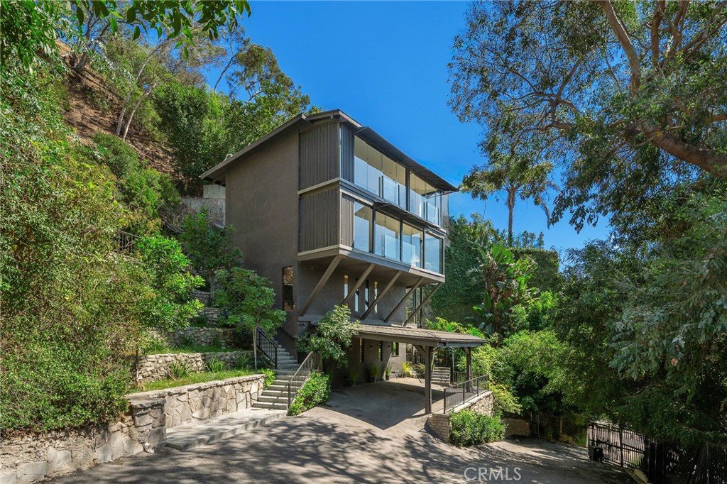 Perched high above the Sunset Strip, this newly reimagined sleek and sculptural, Roger Davis designed VIEW home, embodies elevated living- where form, function, and emotion converge. Truly, a One of a Kind home. Privately gated on a cul de sac street, and surrounded by enormous trees, the setting is both peaceful and practical, with a terraced flat grassy yard, large stone patio, and parking for up to six cars- including a two car SUV ready carport. Thoughtfully restructured from the ground up, the home spans three distinct bedroom levels which are all en suite, including a private entry lower suite ADU with a kitchenette, ideal for guests, additional income, or creative use. A unique 20-foot Cargo Lift rises effortlessly from the carport level to the living room, yard, and patio area. The main level is anchored by a sleek and oversized kitchen island, wide plank floors, 30 feet across of floor to ceiling glass, and sweeping VIEWS from the city to the sea and beyond. Every detail was considered: new copper plumbing, 200-amp panel with dimmable lighting, full rewiring, all-tempered windows, and a brand new HVAC system. Wide plank light oak floors carry warmth throughout, paired with soft recessed lighting and solid-core doors trimmed in stainless steel. The upper level primary suite is a private sanctuary, featuring two bathrooms, a fireplace, dressing room, its own laundry, additional closet space and a sitting area- framed by a dramatic 30 foot glass wall with ocean VIEWS. The lower guest suite offers equal comfort, with its own quaint terrace, fireplace, large dual closets, sitting area, and second washer/dryer space. On the third and bottom level is an ADU. With its own entrance, you’ll find the perfect space ready to serve as a guest quarter, gym, or guest quarters, office, create space, and more. Structural integrity was paramount in this creation. Not Just A Home but a STATEMENT in Hollywood Hills...a rare expression of unique contemporary design, engineered for those who value privacy, craftsmanship and timeless architecture, in the most coveted hillside pocket of Los Angeles.