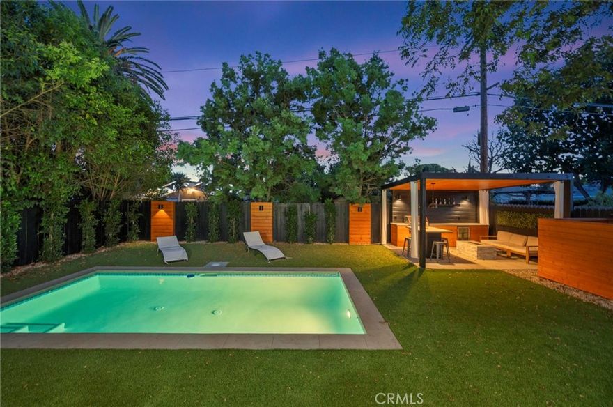 Tucked away on a lush, tree-filled lot, this modern retreat offers the perfect balance of privacy and resort-style living. A remote-controlled iron gate opens to reveal a beautifully reimagined 5-bedroom, 4-bathroom home showcasing timeless design and high-end upgrades throughout. Inside, the open-concept floor plan is anchored by White Oak hardwood floors and a sleek designer kitchen with quartz countertops, under-lit cabinetry, matching Thor appliances, and a built-in three-temperature wine refrigerator. The expansive primary suite overlooks the serene backyard and features a spacious walk-in closet along with a spa-inspired ensuite highlighted by dual sinks and a curb-less, zero-entry shower. Three additional designer bathrooms echo the same attention to detail with walk-in showers and luxury finishes. Step outside to your private paradise: a brand-new sparkling pool shaded by mature trees and complemented by a resort-style cabana. Designed for entertaining, the cabana is complete with an outdoor kitchen, built-in Spires BBQ, dual-temperature wine fridge, mounted TV, overhead lighting, and a cozy fire pit. Recent upgrades provide peace of mind, including a new roof, HVAC system, water heater, all-new copper and PEX plumbing, smooth stucco exterior, stamped concrete driveway, and low-maintenance synthetic turf in both the front and back yards. A rare blend of sophistication, comfort, and modern California living, this home is a true retreat designed for both relaxation and entertaining.