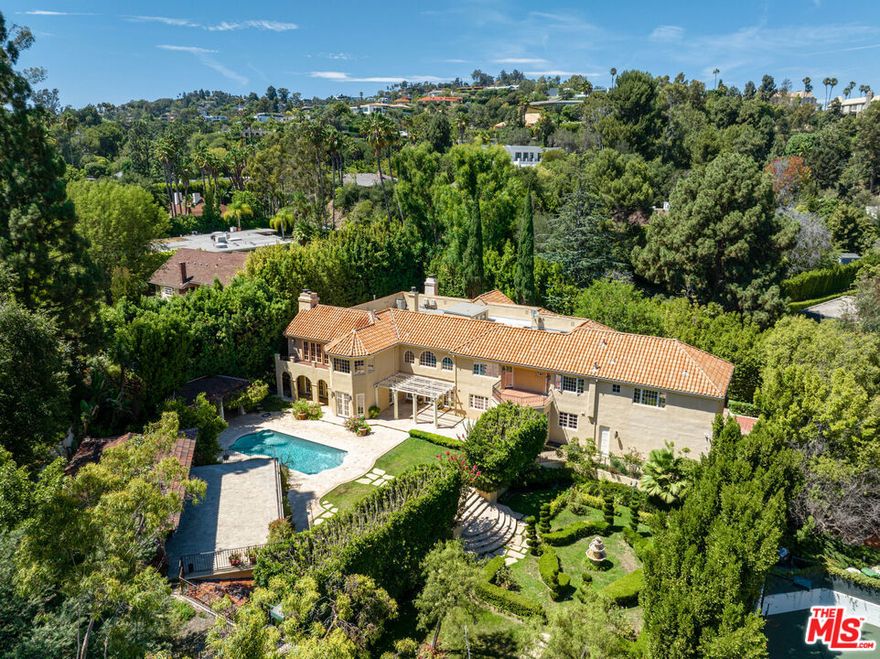 Nestled behind grand gates in one of Beverly Hills' most prestigious neighborhoods, lies a Mediterranean estate of unparalleled grandeur. The compound, with its manicured landscaping, offers the ultimate in privacy and seclusion, allowing for the full enjoyment of the custom pool, spa, sports court, and tended garden. Upon entering the double-height foyer, one is immediately struck by the opulence of the mahogany wood-paneled library, formal living and dining rooms, and the grandeur of the eat-in kitchen complete with full-size butler's pantry. The estate also boasts a gym and wine cellar, catering to the tastes of the most discerning individuals. The primary suite, a true sanctum of luxury, features a stunning chandelier, wood-burning fireplace, spectacular balcony, and dual exquisite custom bathrooms  with walk-in closets. There are five additional en-suite bedrooms upstairs, along with an upstairs family room. Completing this idyllic compound is a detached guest house with a full kitchen, two bedrooms, one bathroom, and a rooftop cabana offering panoramic views of the estate. Host grand events in the expansive public spaces or retreat to the bedrooms for a moment of opulence, either way, 1055 Shadow Hill Way is a true embodiment of ethereal living