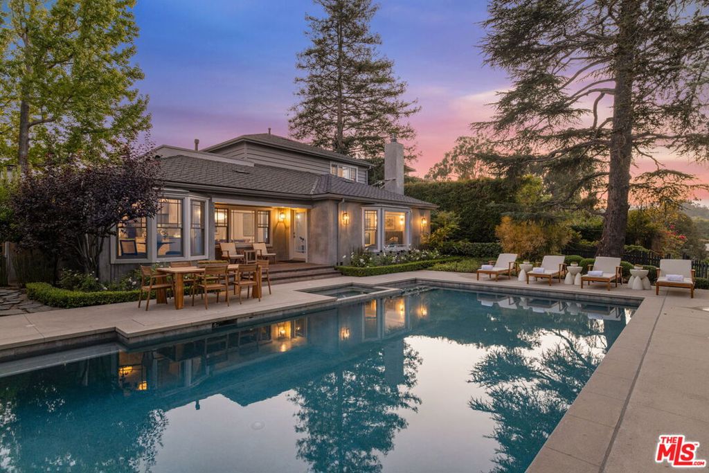 Tucked away at the end of a serene cul-de-sac in one of Brentwood's most desirable enclaves, this gated 5-bedroom, 5.5-bath residence blends the grace of timeless architecture with the easy sophistication of California living. Wrapped in mature, fragrant greenery, the home offers seclusion, warmth, and sunlight in every room. Designed with an eye for harmony by interior designer Nancy Whaley, the interiors welcome you with rich dark hardwood floors, soft textures, and grand picture windows framing the surrounding gardens. In the living room, a dramatic stone fireplace creates a natural gathering place, flowing seamlessly into the formal dining room where leafy views set the mood for intimate dinners. The chef's kitchen, bathed in light, boasts premium appliances, a casual dining nook, and an effortless layout for cooking, entertaining, or simply lingering over morning coffee. The spacious family room anchored by a sleek modern fireplace opens through French doors to the manicured front garden, where the gentle splash of a fountain invites moments of calm. The first-floor primary suite is a private escape, complete with a spa-like bath and soaking tub perfectly positioned beneath a broad picture window. A nearby guest bedroom with custom built-in shelving offers both beauty and practicality. Upstairs, secondary bedrooms, each with its own bath, are airy and light-filled, ideal for guests, children, or creative pursuits. Outdoors, a sparkling pool and spa are framed by lush trees and vibrant blooms, with enchanting canyon views that make you feel a world away yet you're only minutes from Brentwood Village, acclaimed schools, and the best of the Westside. A separate one-bedroom, one-bath guest studio completes the estate, providing a private space for visitors, an inspiring work retreat, or a serene getaway. This is California living at its most refined effortlessly blending comfort, style, and the magic of indoor-outdoor life.