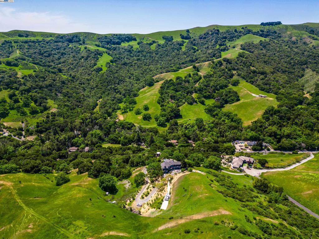 Located in an exclusive gated community and perched atop a scenic hill, this 2022-renovated retreat sits on 5 picturesque acres, blending luxury and nature just minutes from town. The 3,500 sq ft home offers 4 bedrooms, 4.5 bathrooms, an office, panoramic valley views, complete privacy, and backs to over 2,500 acres of parkland. High-end finishes include a hand-forged iron staircase and floor-to-ceiling windows that frame the landscape. The chef’s kitchen features a stainless steel refrigerator, six-burner range with griddle and pot filler, double ovens, microwave, quartz waterfall island, and custom cabinetry. The dining room opens to the outdoors through glass doors and includes a stone counter for entertaining. Bedrooms feature California Closets and spa-like bathrooms with floor-to-ceiling tile and heated floors. The primary suite has a walk-in closet with illuminated displays, dual vanities, and hillside views. A second en-suite offers privacy for guests or multi-gen living. Expansive wraparound decks reveal views of Bollinger Canyon and lead to a sunroom with sink and stainless counter, perfect for hobbies. A generator provides energy backup. Adjacent lots 315 & 0 Bollinger Estates Ct may be purchased together as a rare 17-acre estate.